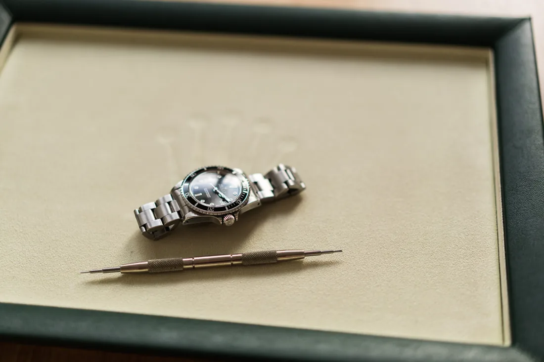 Rolex Submariner mit Stahlband und Federsteg-Werkzeug auf dem Polster einer Rolex-Box