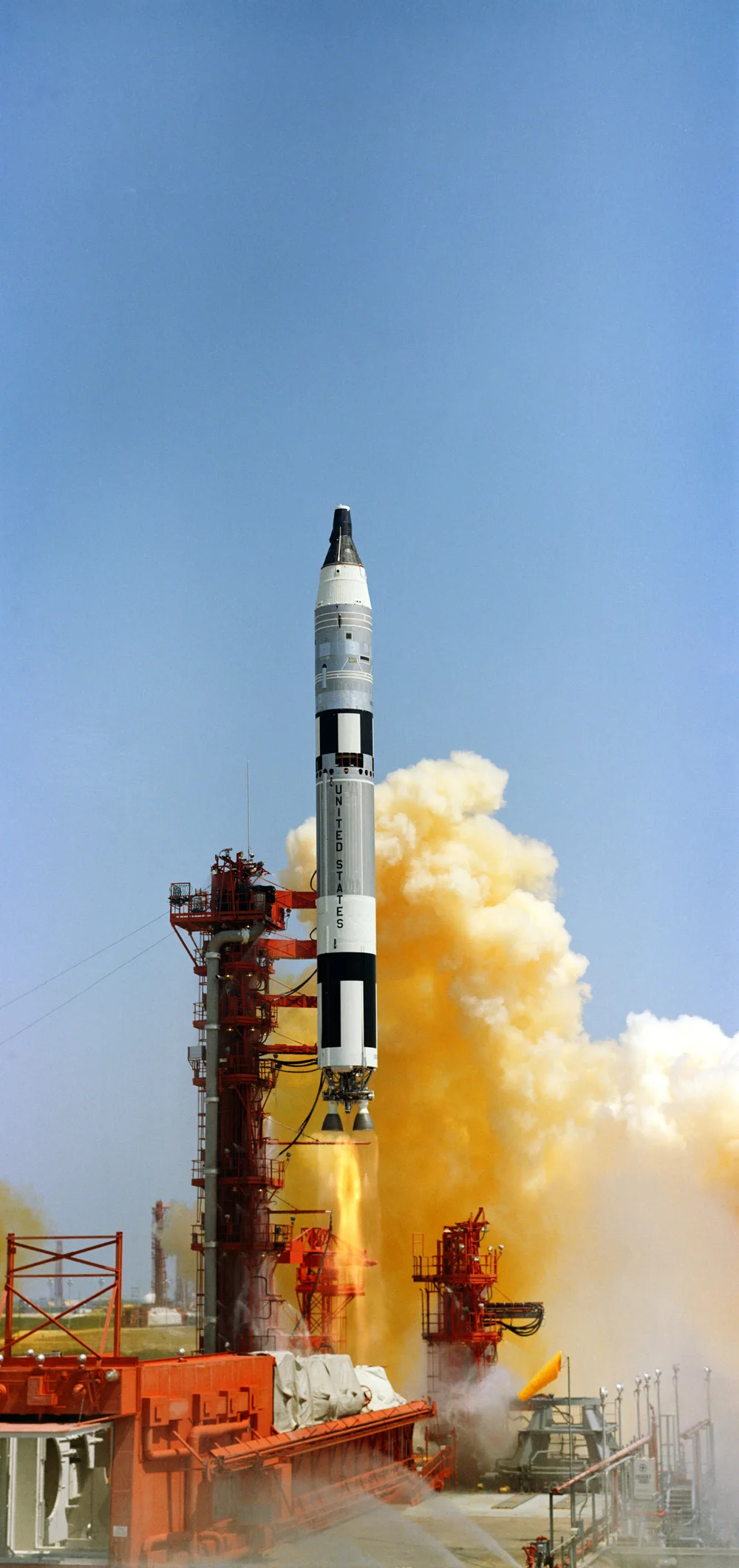 Launch of the Gemini-Titan 4 rocket, with a red launch tower on the left and orange smoke rising on the right